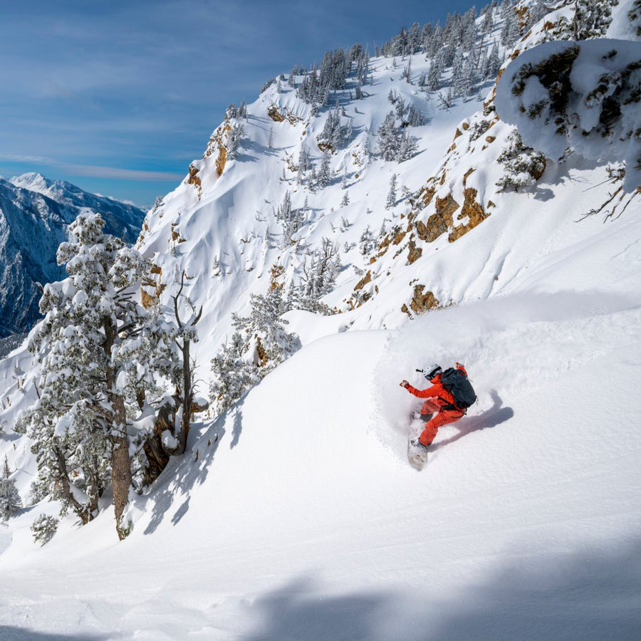 A snowboarder heel turns down a couloir.