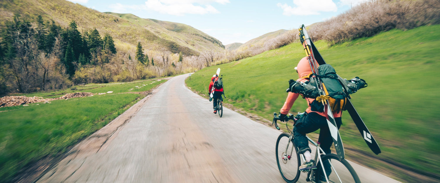 Two skiers ride their bikes up a green canyon