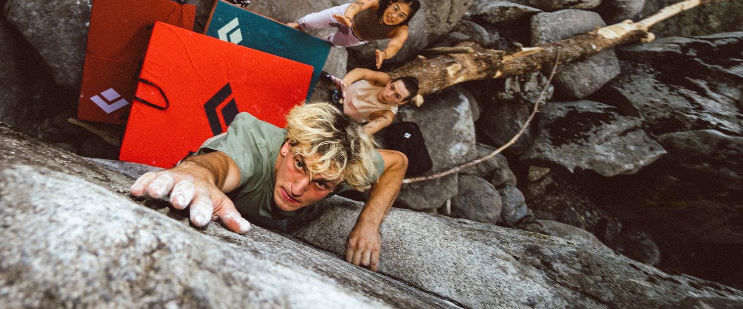 A boulder reaches for a hold with friends onlooking