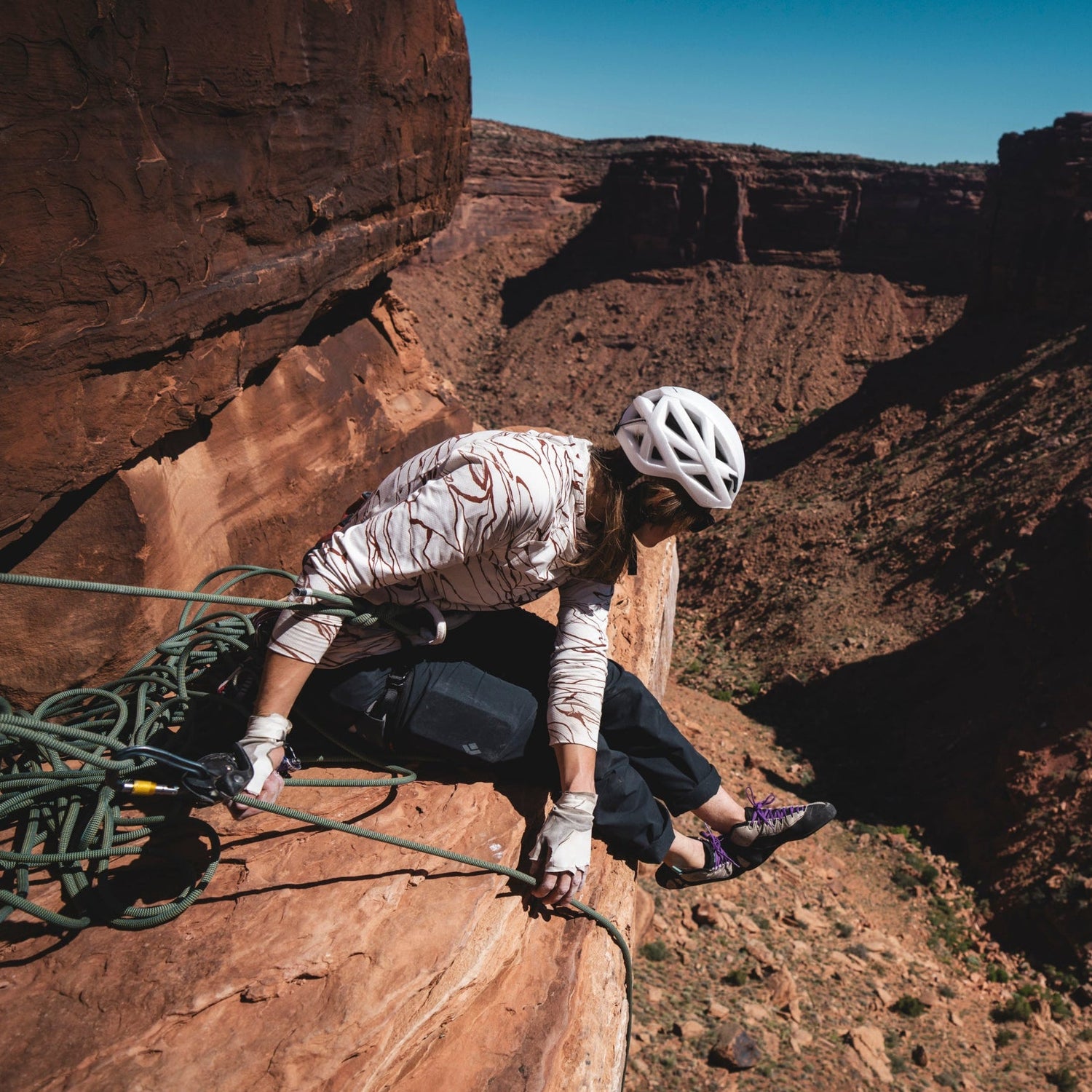 A climber in a sun hoody, belaying on a desert ledge.