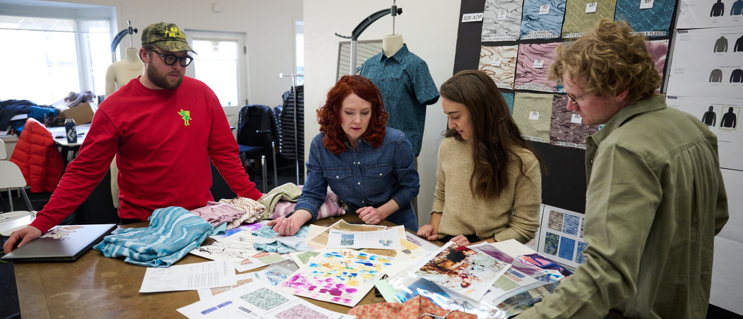 Four people in a design studio looking at fabric samples and designs on a table.